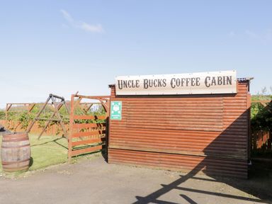 An outdoor wooden coffee cabin with a sign uncle bucks coffee cabin and a wooden swing set next to it at Whiskey Creek Cabin in Castlerock