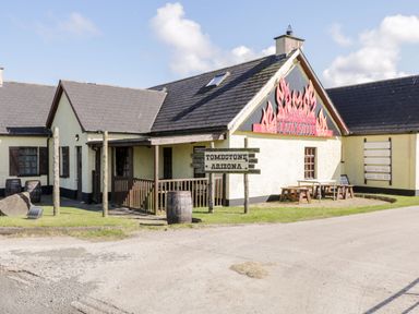 A building with a sign reading the blazin saddle and a wooden sign saying tombstone arizona with barrels and outdoor tables on grass at Whiskey Creek Cabin in Castlerock