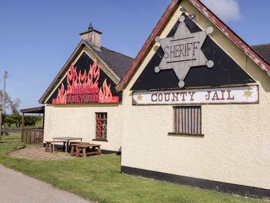 A building with signs reading sheriff county jail and the blazin saddle with outdoor picnic tables