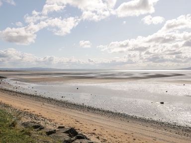 A sandy beach with shallow water and rocks under a cloudy sky at Whiskey Creek Cabin in Castlerock