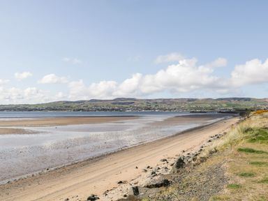 A sandy beach with rocks along the shore and a body of water with hills and houses in the background at Whiskey Creek Cabin in Castlerock