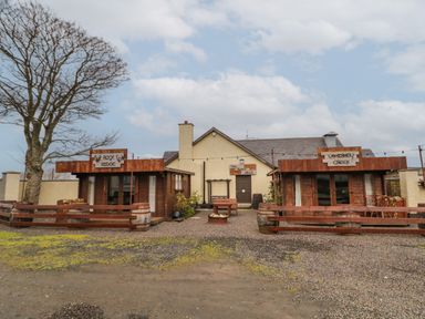 A courtyard with two wooden cabins and a cream building in the background at Whiskey Creek Cabin in Castlerock