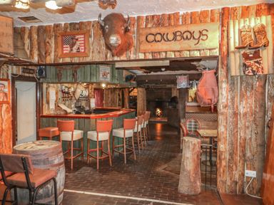 A rustic bar area with wooden stools a mounted buffalo head and cowboy decorations at Whiskey Creek Cabin in Castlerock