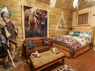 A bedroom with a bed patterned blanket wooden bench coffee table with skulls and a large native american statue at Apache Falls Lodge in Castlerock