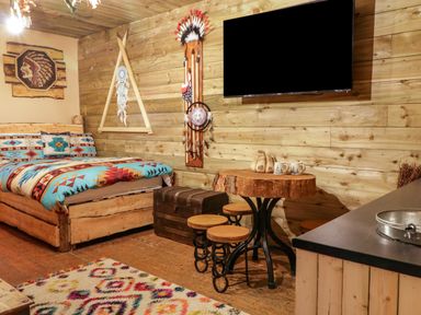 A bedroom with a wooden bed with patterned bedding a wooden table with stools a wall-mounted TV and rustic decor at Apache Falls Lodge in Castlerock