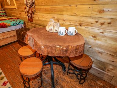 A rustic wooden table with three round stools cups and a wooden pumpkin against a wood paneled wall at Apache Falls Lodge in Castlerock