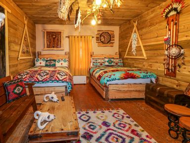 A bedroom with two beds wooden walls wooden coffee table with skulls bench and native American decorations at Apache Falls Lodge in Castlerock