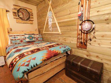 A bedroom with a bed with patterned bedding a wooden wall with dreamcatchers and a wooden chest at Apache Falls Lodge Castlerock