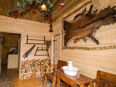 A wooden room with stacked firewood saw hanging on wall a wash basin on a wooden bench and an animal hide on the wall at Apache Falls Lodge in Castlerock