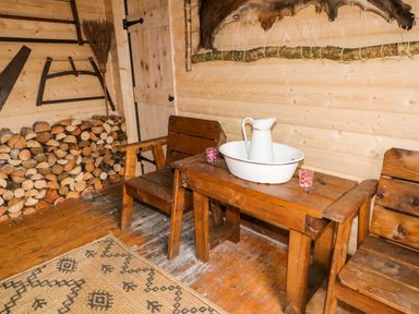 A wooden room with stacked firewood chairs a table with a white pitcher and basin at Apache Falls Lodge in Castlerock