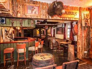 A rustic bar area with wooden stools a wooden barrel table and western decor including a buffalo head and cowboy picture at Apache Falls Lodge in Castlerock