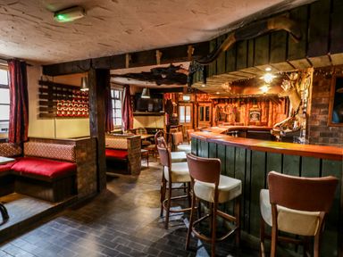 An interior view of a bar with wooden chairs and booths with red cushions at Apache Falls Lodge in Castlerock