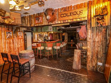 A rustic bar area with wooden walls and stools a mounted buffalo head and cowboy themed decorations at Apache Falls Lodge in Castlerock