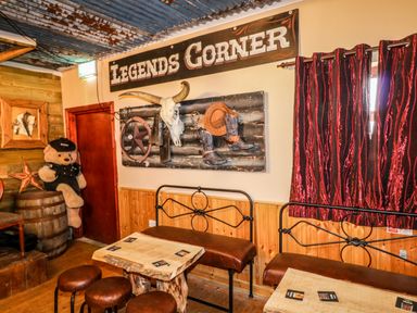 A rustic room with wooden tables and stools a teddy bear sitting on a barrel wall decor including a steer skull boots and a hat at Apache Falls Lodge in Castlerock