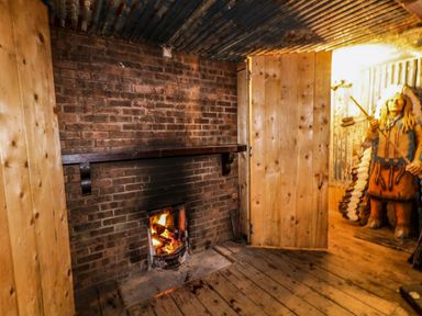 A room with a brick fireplace burning wood and a wooden figure of a Native American statue at Apache Falls Lodge in Castlerock