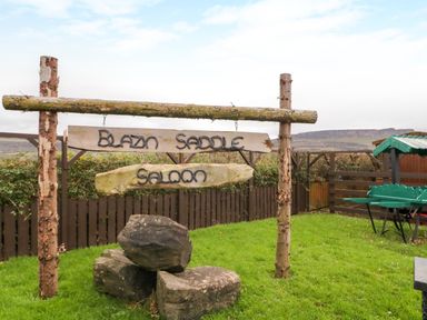 A wooden sign reading Blazin Saddle Saloon in a grassy fenced yard at Apache Falls Lodge in Castlerock