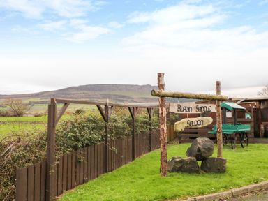 A grassy area with a wooden sign reading Blazin Saddle Saloon and large rocks near a wooden fence and green cart