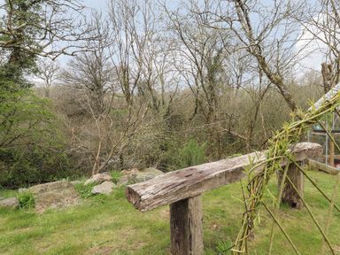 A wooden bench on grass with bare trees and rocks in the background at Mill Cabin Denant in Haverfordwest