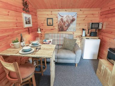 A small wooden cabin interior with a dining table set for two a sofa a mini fridge and a microwave at Mill Cabin Denant in Haverfordwest