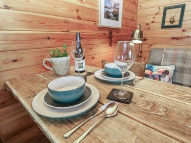 A wooden dining table set for two with bowls plates wine glasses cutlery a potted plant and a bottle of wine in a wooden room at Mill Cabin Denant in Haverfordwest