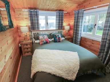 A bedroom with a double bed two bedside tables lamps and plaid curtains at Mill Cabin Denant in Haverfordwest