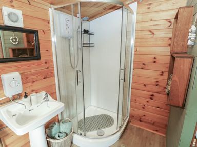 A bathroom with a corner shower enclosure a white pedestal sink a basket with rolled towels and wooden wall shelves at Mill Cabin Denant Haverfordwest