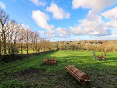 A grassy field with farm equipment and trees under a blue sky at Audrey in Penzance near Newlyn