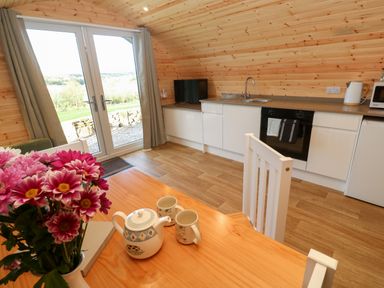 A kitchen with white cabinets and wood paneled walls near a table with a teapot cups and flowers at Audrey in Penzance near Newlyn