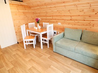 A dining table with four chairs and flowers on it next to a green sofa in a wooden room at Audrey in Penzance near Newlyn