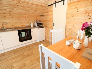 A kitchen with wooden walls a dining table white chairs and kitchen appliances at Audrey in Penzance near Newlyn