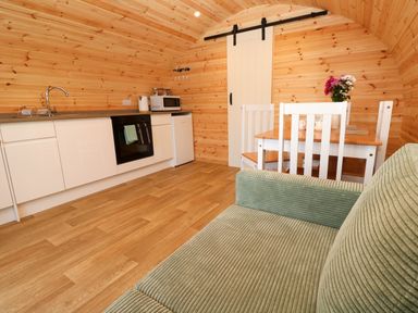 A wooden kitchen and dining area with white cabinets stove microwave fridge green sofa and table with chairs at Audrey in Penzance near Newlyn