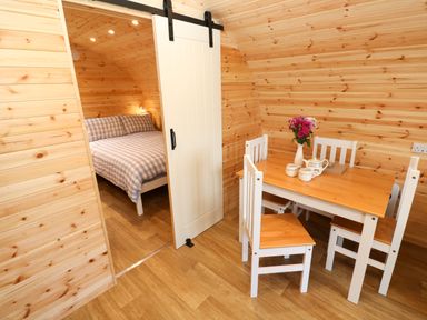 A wooden dining table with chairs and flowers next to a bedroom with a bed behind a sliding door at Audrey Penzance near Newlyn