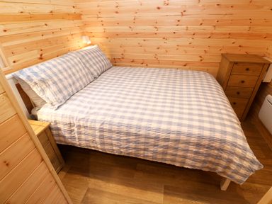 A bedroom with a bed with checked bedding and two wooden bedside cabinets at Audrey in Penzance near Newlyn