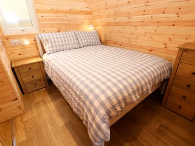 A bedroom with a bed covered in checkered bedding and wooden furniture at Audrey in Penzance near Newlyn
