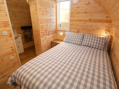 A bedroom with a bed with checked bedding and wooden walls at Audrey in Penzance near Newlyn