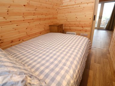 A bedroom with wooden walls a bed with checkered bedding and a small wooden nightstand at Audrey in Penzance near Newlyn