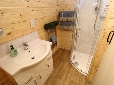 A bathroom with a sink, towel rack with towels, and a curved glass shower at Audrey in Penzance near Newlyn