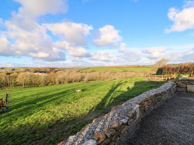 A stone wall with gravel beside a green grassy field and trees under a blue sky at Audrey in Penzance near Newlyn