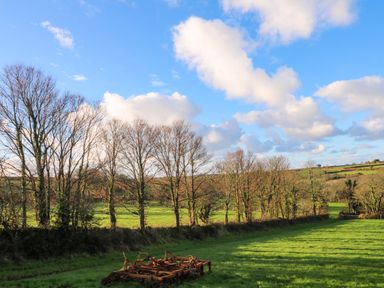 A green field with farming equipment and trees under a blue sky at Audrey in Penzance near Newlyn