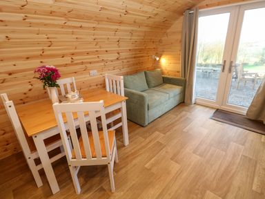 A wooden interior room with a dining table and chairs next to a green sofa and glass doors at Lloyd in Penzance near Newlyn