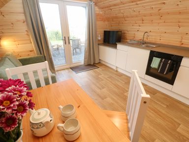 A kitchen and dining area with a wooden table and chairs a green sofa a countertop with a sink and oven and glass doors leading outside at Lloyd in Penzance near Newlyn
