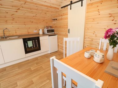 A kitchen with wooden walls and floor with a dining table with a tea set and flowers at Lloyd in Penzance near Newlyn