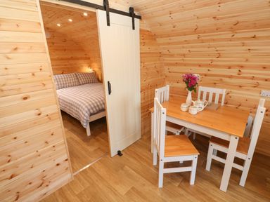 A wooden room with a dining table and chairs and a bed visible through a sliding door at Lloyd in Penzance near Newlyn