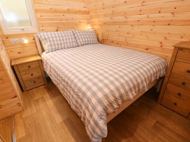 A bedroom with a bed with checkered bedding and wooden drawers on each side at Lloyd in Penzance near Newlyn