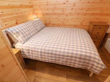 A bedroom with a double bed featuring checkered bedding and two wooden bedside cabinets at Lloyd in Penzance near Newlyn