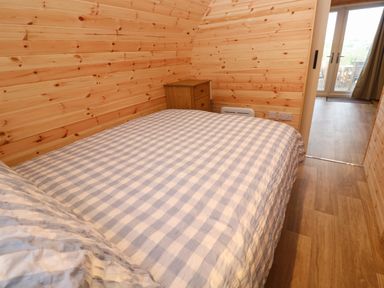 A bedroom with wooden walls a bed with checkered bedding a wooden nightstand and a door leading outside at Lloyd in Penzance near Newlyn