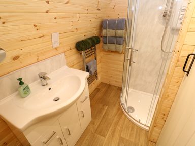 A bathroom with a white sink cabinet towel rack and a corner glass shower at Lloyd in Penzance near Newlyn