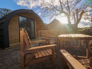 An outdoor seating area with wooden chairs and a table in front of a small wooden cabin with double doors at Lloyd in Penzance near Newlyn