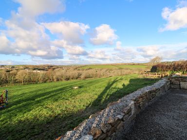 A grassy field with a stone wall and wooden fence under a blue sky at Lloyd in Penzance near Newlyn