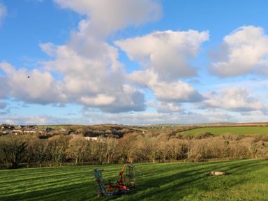 A grassy field with a piece of farming equipment and houses on a hillside at Lloyd in Penzance near Newlyn